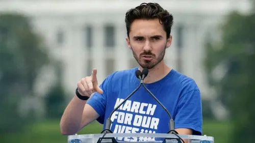 ديفيد هوغ يتحدث في تجمع عام، مرتديًا قميصًا أزرق مكتوب عليه "مارش من أجل حياتنا"، مع خلفية غير واضحة لمكان الحدث.