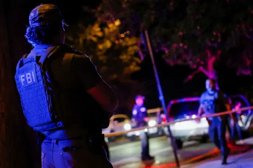 عميل من مكتب التحقيقات الفيدرالي يرتدي سترة واقية، يقف في موقع حادث، بينما يتواجد ضباط آخرون في الخلفية خلال عملية اعتقال.