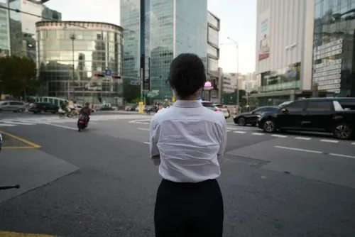 امرأة ترتدي قميصًا أبيض وسروالًا أسود، تقف في الشارع أمام ناطحات سحاب في مدينة حديثة، تعكس التحديات التي تواجهها ضحايا الجرائم الجنسية الرقمية.