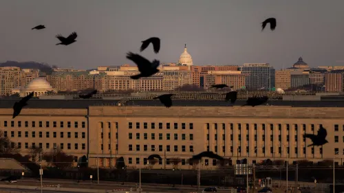 مبنى البنتاغون مع طيور تحلق في السماء، بينما تظهر معالم العاصمة واشنطن في الخلفية، مما يعكس أهمية القضايا العسكرية والأمنية.