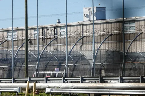 مركز احتجاز مهاجرين محاط بأسلاك شائكة، يظهر فيه المبنى الفيدرالي مع علامات تحذيرية، يرمز إلى قضايا الرقابة والممارسات القانونية.