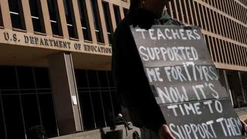 محتج يحمل لافتة أمام وزارة التعليم الأمريكية، يطالب بدعم المعلمين بعد تسريحات جماعية للموظفين، في سياق دعوى قضائية ضد الإدارة.