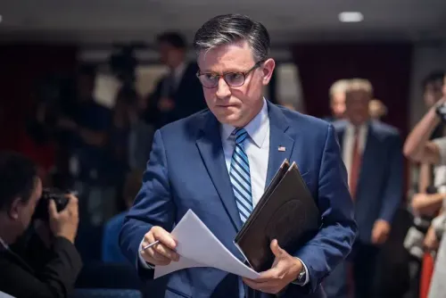 رجل يرتدي بدلة رسمية يحمل أوراقًا، يبدو جادًا أثناء مغادرته قاعة مؤتمرات، مما يعكس أجواء السياسة الأمريكية الحالية.