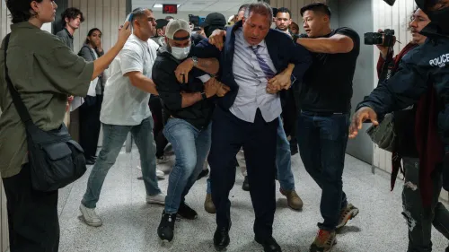 اعتقال مسؤول حكومي وسط احتجاجات على سياسات الهجرة، مع تواجد حشد من المتظاهرين والمصورين في الخلفية.