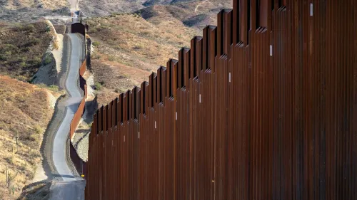 جدار حدودي يمتد عبر تلال جافة، يمثل جزءًا من النقاش حول قوانين الهجرة الجديدة في الولايات المتحدة.