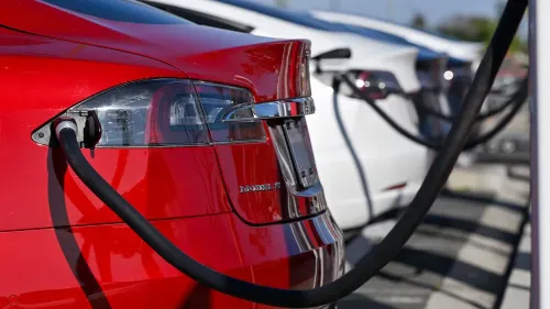 سيارة كهربائية حمراء متصلة بشاحن، مع سيارات أخرى في الخلفية، تعكس جهود كاليفورنيا للحد من انبعاثات السيارات.