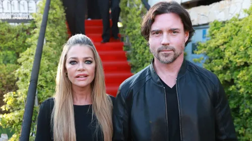 دينيس ريتشاردز وآرون فيبرز يقفان معًا في حدث عام، حيث تظهر ريتشاردز بوضوح مع علامات على وجهها تشير إلى إصابة.