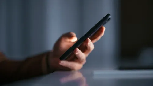 يد تحمل هاتفا ذكيا مضاء في بيئة مظلمة، مما يعكس القلق حول استخدام الذكاء الاصطناعي في إنشاء محتوى مزيف.