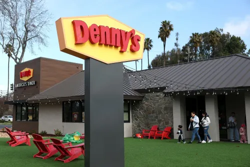 لافتة مطعم دينيز تظهر اسم المطعم "Denny's" مع عائلات تتجول في الخارج، تعكس التحديات التي تواجهها السلسلة في السوق.