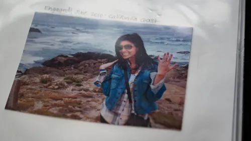 صورة لإيلين غرينبرغ، معلمة مدرسة، مبتسمة وترتدي سترة زرقاء، تشير بإصبعها إلى خاتم الخطوبة، بينما تظهر خلفها شواطئ كاليفورنيا.