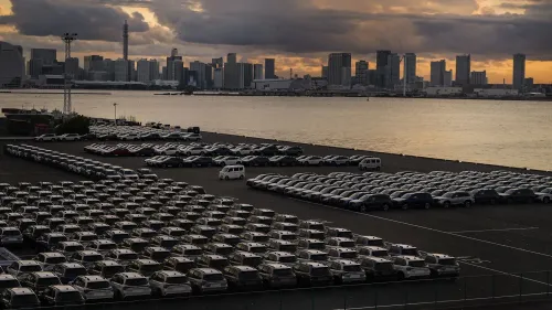 صف من السيارات في ميناء ياباني مع أفق المدينة في الخلفية، يعكس التوترات التجارية بين الولايات المتحدة واليابان في صناعة السيارات.