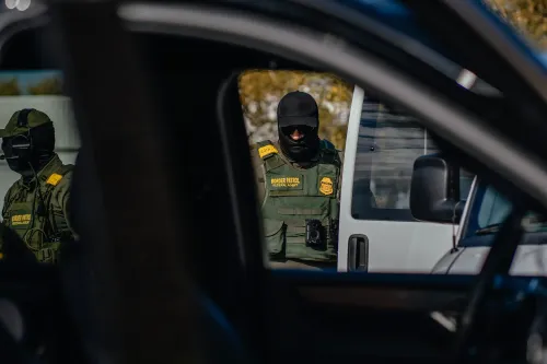 عناصر من إدارة الهجرة يقفون بالقرب من سيارة أثناء مداهمة، مما يعكس التوترات المحيطة بقضايا الهجرة في الولايات المتحدة.