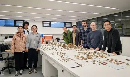 فريق من الباحثين يقف أمام طاولة مليئة بالأدوات الحجرية المكتشفة في موقع لونغتان في الصين، مما يدل على تقنيات إنسان النياندرتال.