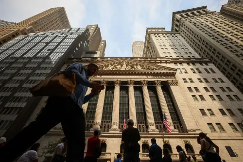 واجهة بورصة نيويورك مع أشخاص يسيرون في المقدمة، تعكس النشاط المالي وتأثير الأسواق الخاصة على الاستثمارات.