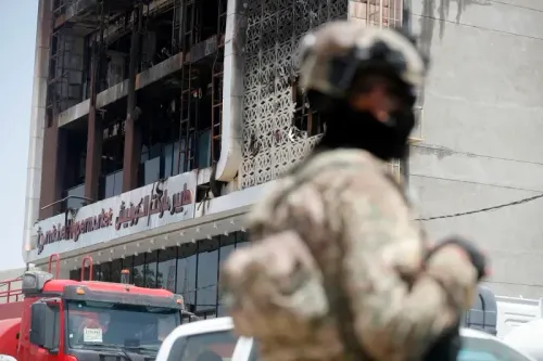 مركز تسوق محترق في مدينة الكوت بالعراق، مع وجود رجال أمن في المقدمة، بعد الحريق الذي أودى بحياة 61 شخصًا.