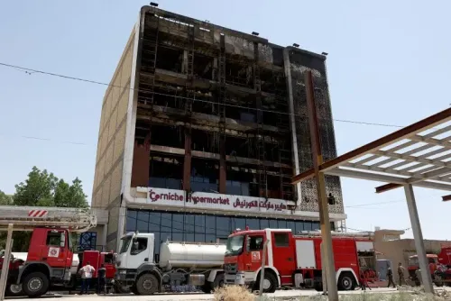 مبنى هايبر ماركت الكورنيش المتضرر من حريق هائل في الكوت، مع وجود سيارات إطفاء في الموقع بعد جهود الإنقاذ.