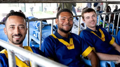 ثلاثة أمريكيين مبتسمين يرتدون زيًا برتقاليًا وأزرق، يجلسون في صف من الكراسي الزرقاء، في سياق تخفيف أحكام الإعدام عنهم في الكونغو.