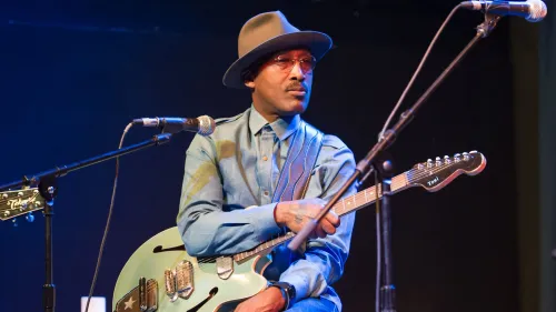 دي واين ويجينز، عازف الجيتار والمغني في فرقة R&B توني! توني! توني!، يظهر أثناء أداء موسيقي، معزياً تاريخه الفني الغني.