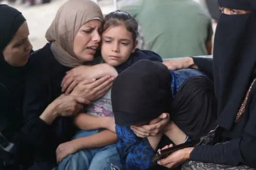 نساء وأطفال فلسطينيون يجلسون معًا في حالة من الحزن، يعبرون عن مشاعر القلق والألم بسبب الوضع الراهن في غزة.