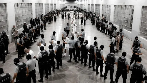 مشهد من داخل سجن سيكوت في السلفادور، حيث يتجمع حراس مسلحون حول سجناء يرتدون ملابس بيضاء، وسط أجواء مشددة.