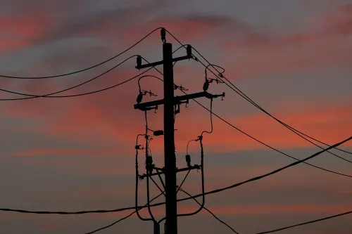 أعمدة كهرباء silhouetted against سماء غروب الشمس، تعكس التحديات المتزايدة في تكاليف الطاقة والكهرباء في الولايات المتحدة.