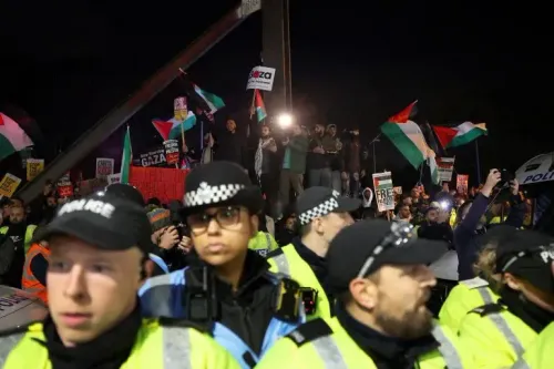 تظهر الصورة مجموعة من المحتجين يحملون أعلام فلسطين ولافتات في مظاهرة خارج ملعب فيلا بارك، مع وجود شرطة تحرس المنطقة.