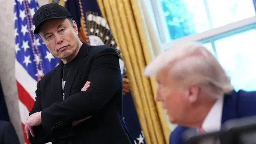 إيلون ماسك يتأمل بجدية بينما ينظر ترامب إلى الأمام، مع العلم الأمريكي خلفهم، خلال حديث حول التشريعات المثيرة للجدل.