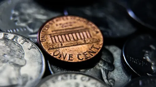 صورة لنقود معدنية تظهر بنسًا أمريكيًا مميزًا موضوعًا بين عملات أخرى، مما يعكس المناقشات حول جدوى العملة المعدنية.