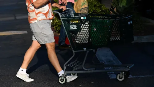 رجل يحمل عربة تسوق من متجر Whole Foods، بينما تظهر خلفه أرفف فارغة، مما يعكس تأثير الهجوم الإلكتروني على المخزون.