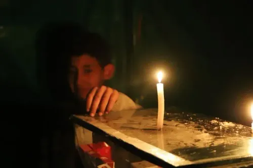 طفل يجلس في الظلام بجوار شمعة مضاءة، معبرًا عن معاناة سكان غزة جراء نقص الكهرباء وسط الأزمة الإنسانية المتفاقمة.