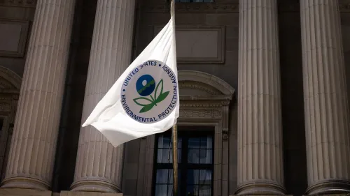 علم وكالة حماية البيئة يرفرف أمام مبنى الإدارة، مع أعمدة معمارية بارزة، مما يرمز إلى التحديات التي يواجهها الموظفون تحت الاختبار.