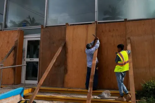 عمال يقومون بتثبيت الألواح الخشبية على واجهة مبنى في أكابولكو استعداداً لإعصار إريك، مع وجود معدات وأدوات حولهم.