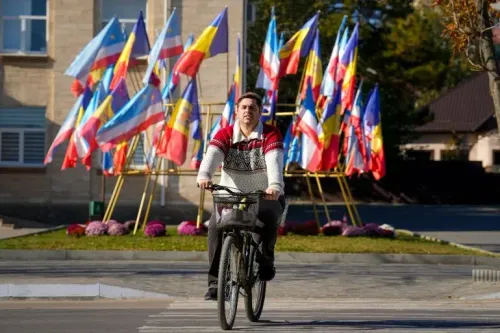 رجل يركب دراجة أمام مجموعة من الأعلام الملونة في مولدوفا، تعكس دعم البلاد للانضمام إلى الاتحاد الأوروبي وسط توترات سياسية.