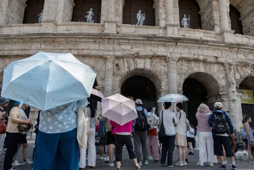 سياح يحملون مظلات واقية من الشمس أمام الكولوسيوم في روما، وسط موجة حرّ قياسية تؤثر على أوروبا.