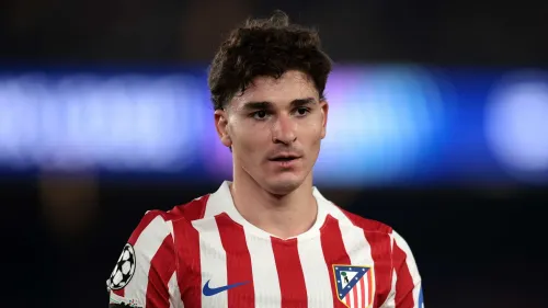 جوليان ألفاريز لاعب أتلتيكو مدريد يرتدي قميص الفريق الأحمر والأبيض خلال مباراة، وسط تكهنات حول انتقاله المحتمل إلى برشلونة.