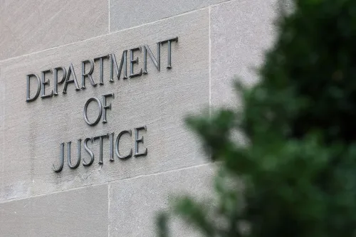 لافتة وزارة العدل الأمريكية مكتوبة على جدار، مع وجود نباتات خضراء في المقدمة، تعكس التغييرات في قيادة المكتب.