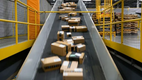 حزم شحن تتدفق على منحدر في مركز توزيع أمازون، تعكس التأثيرات المحتملة للحرب التجارية على الأسعار وتكاليف الشحن.