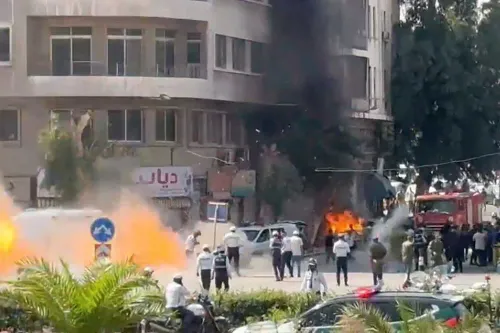 انفجاران قرب فندق فور سيزونز في دمشق أثناء زيارة ماكرون، مع تصاعد الدخان ونيران وسط تجمع عناصر الأمن والمارة.