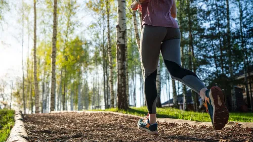 امرأة تجري على ممر محاط بالأشجار، تعكس الصورة أهمية النشاط البدني في تحقيق الصحة والعافية.