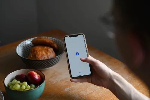 شخص يستخدم هاتفه المحمول لفتح تطبيق فيسبوك، بينما تظهر أطباق من الفواكه والمعجنات على الطاولة، في سياق تسوية متعلقة بخصوصية البيانات.