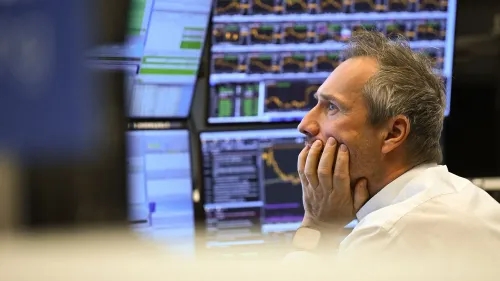 متداول يراقب شاشات متعددة تعرض بيانات السوق المالية، مع تعبير عن القلق بسبب تقلبات الأسهم الأمريكية وتأثير التعريفات الجمركية.