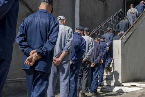 رجال يرتدون ملابس زرقاء يسيرون في صف نحو الدرج، مما يعكس حالة أسرى الحرب الذين تم تجنيدهم بشكل غير قانوني للقتال في أوكرانيا.