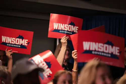 لافتات انتخابية تحمل اسم "وينسوم" مرشحة حاكم ولاية فيرجينيا، تُرفع من قبل مؤيدين في حدث جماهيري.