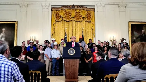 ترامب يتحدث في البيت الأبيض أمام حشد من الناس، مع وجود علم أمريكي خلفه، أثناء مناقشة مشروع قانون السياسة الداخلية.