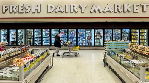 سوق الألبان الطازجة في سوبرماركت، حيث تظهر امرأة تدفع عربة تسوق أمام رفوف مليئة بمنتجات الألبان المختلفة.