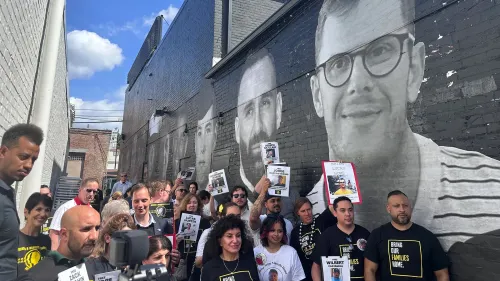 مجموعة من الأشخاص يتجمعون أمام لوحة جدارية ضخمة تعرض صور معتقلين أمريكيين في الخارج، يحملون لافتات للمطالبة بالإفراج عنهم.