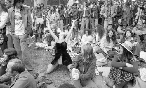 مجموعة من المعجبين بفرقة Grateful Dead يجلسون في حفل موسيقي، بينما تؤدي راقصة في الوسط حركات تعبيرية تعكس روح الاحتفال.