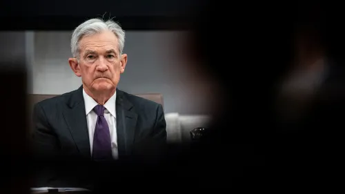 جيروم باول، رئيس الاحتياطي الفيدرالي، يجلس في اجتماع، مع تعبير جاد، في سياق الانتقادات السياسية حول أسعار الفائدة.