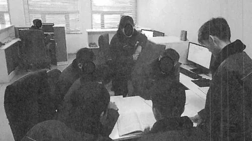 مجموعة من الأشخاص يعملون في مكتب، مع أجهزة كمبيوتر محمولة على الطاولات، في سياق جهود كوريا الشمالية لاستخدام التكنولوجيا عن بعد لتمويل برامجها.