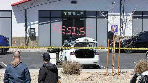 تظهر الصورة واجهة صالة عرض تسلا، حيث كُتبت كلمة "مقاومة" بالطلاء الأحمر، مع وجود سيارات متضررة وأفراد يتفقدون المكان.